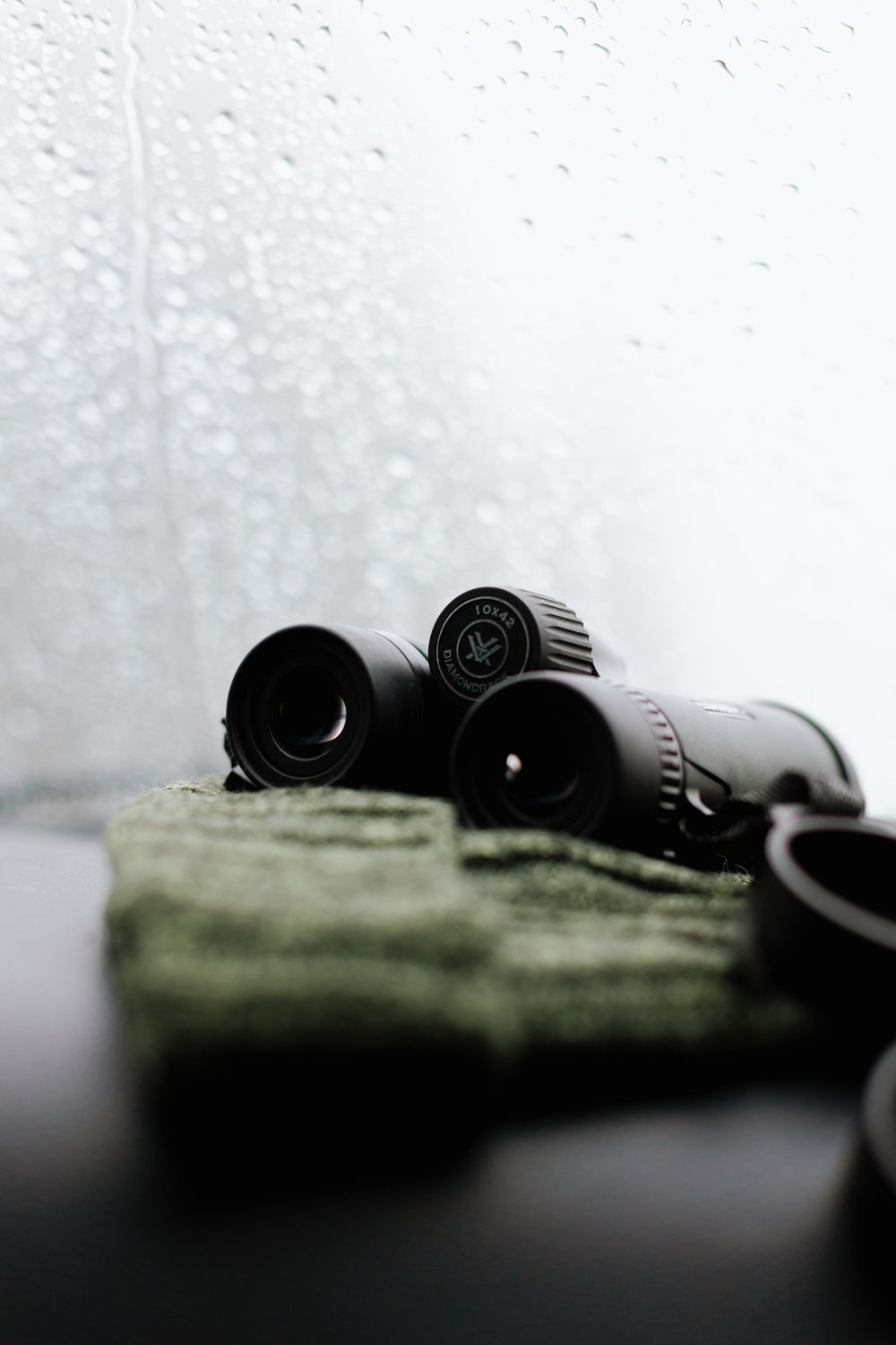 binoculars sitting on top of a green hat on dash of truck with rainy windshield in background