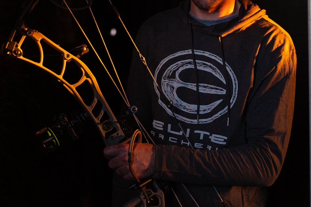orange light highlighting archery bow with man holding it dressed in hoodie
