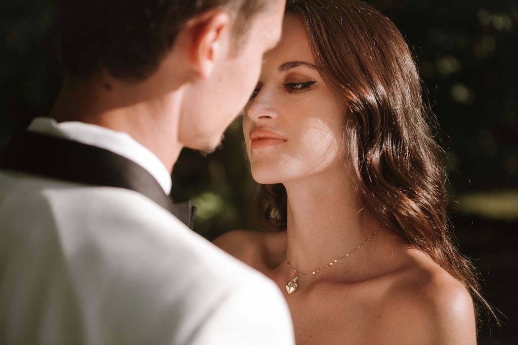 Intimate wedding photo of a couple sharing a romantic moment against a sunlit natural background.