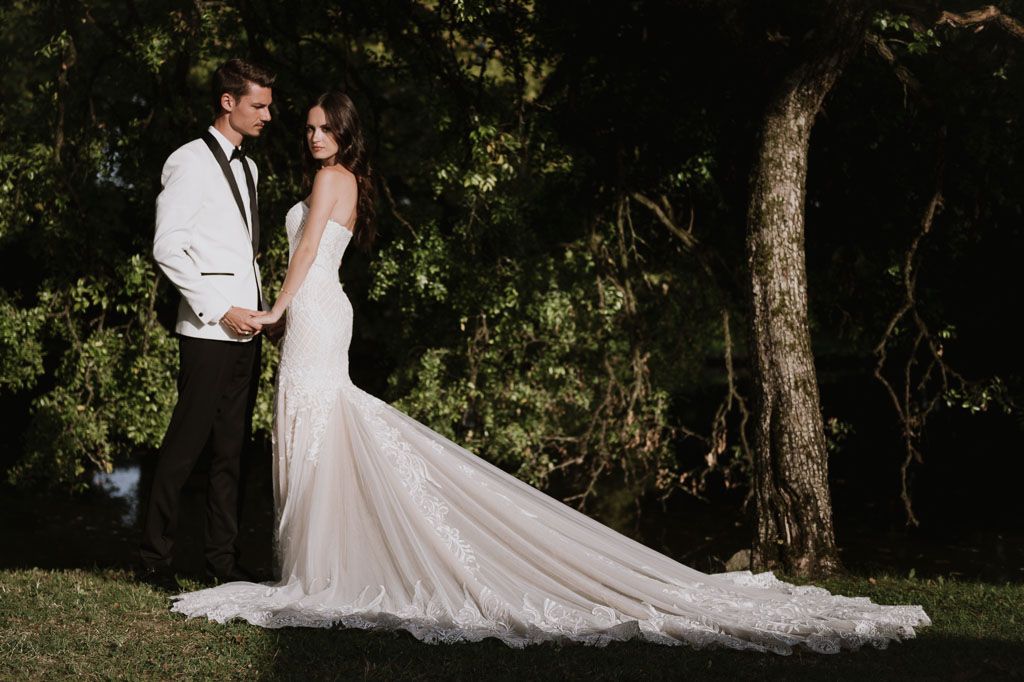 Elegant wedding portrait showcasing a stunning lace train dress against a natural wooded backdrop.