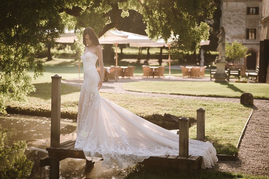 Wedding gown with dramatic train displayed on rustic wooden bridge in garden setting.
