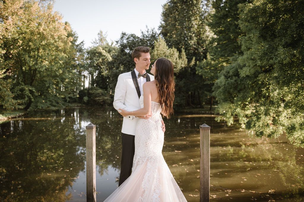 Wedding couple sharing romantic moment on wooden bridge overlooking pond.