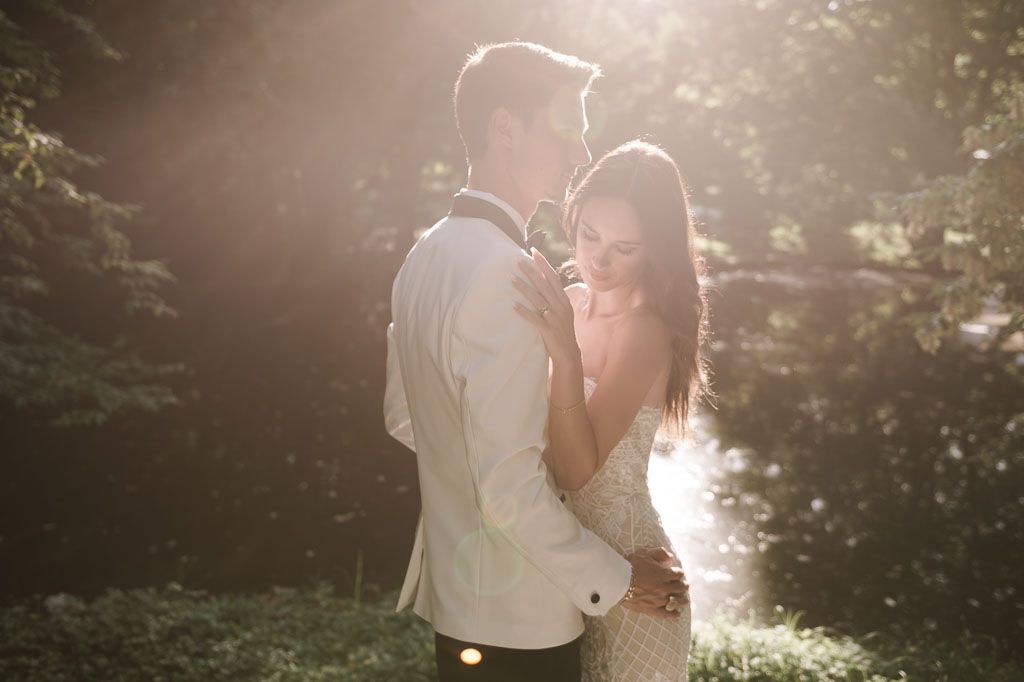 Romantic sunset wedding photo of couple in white attire against glowing forest background.