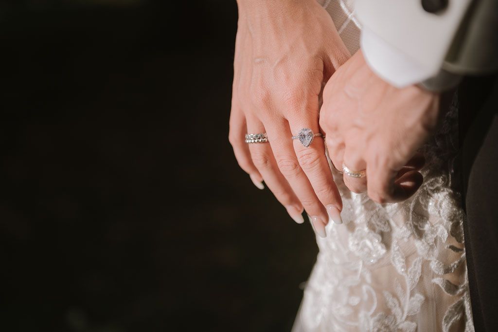 Detail shot of wedding rings and intricate lace on bride's dress.