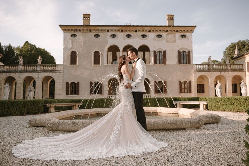 Elegant wedding couple poses by a fountain at an Italian villa with a stunning long train dress.