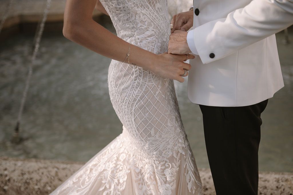 Close-up detail of wedding dress lace and couple's embrace.