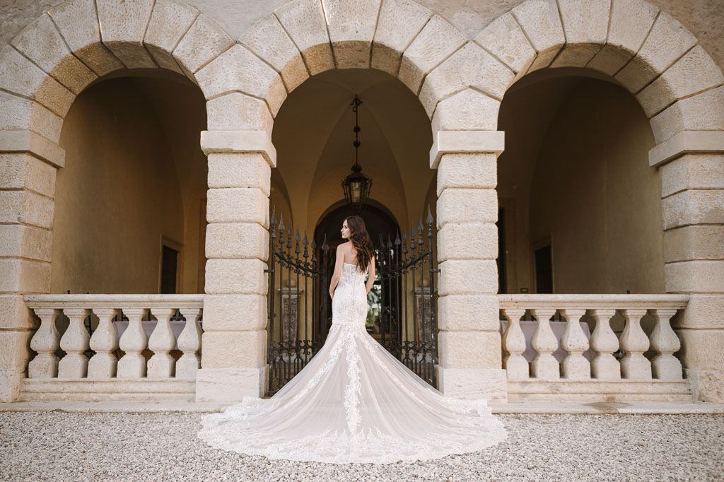 Bride in mermaid wedding dress with long train poses under stone archways.