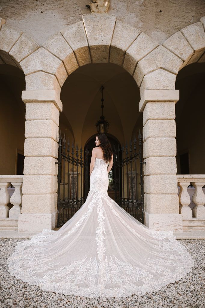 Dramatic bridal portrait showcasing intricate lace train under stone archway.