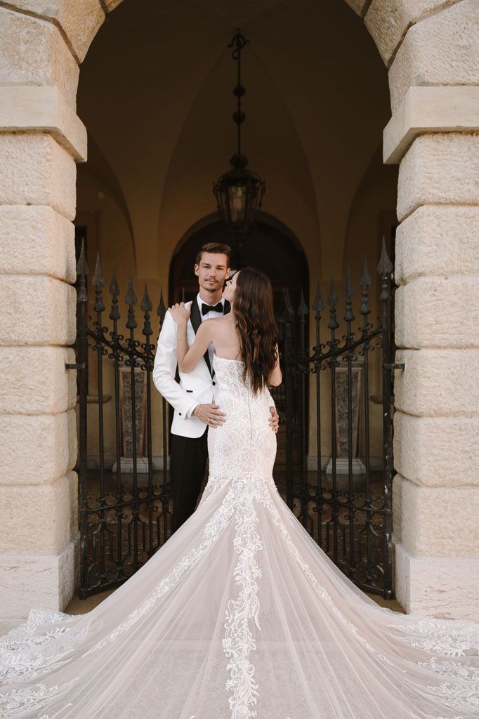 Elegant wedding portrait under stone archway with dramatic train detail.