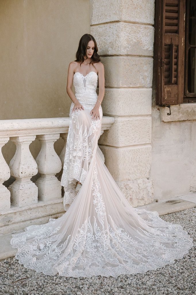 Elegant lace wedding gown with sweetheart neckline and dramatic cathedral train on stone balcony.