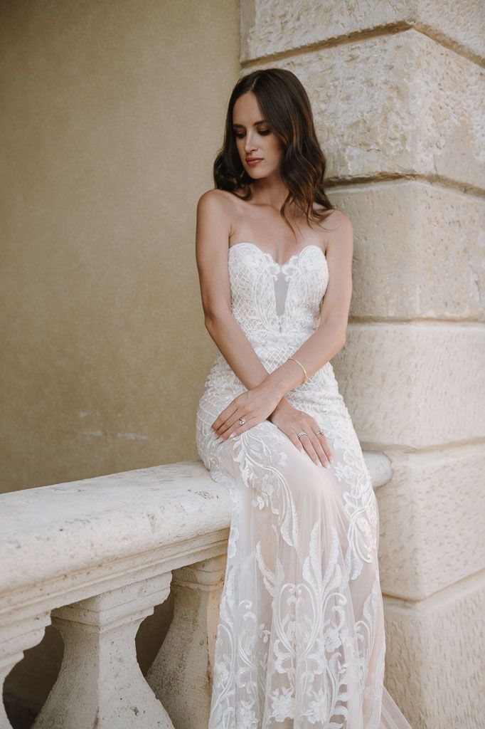 Delicate lace wedding dress showcased against neutral stone architecture and balustrade.