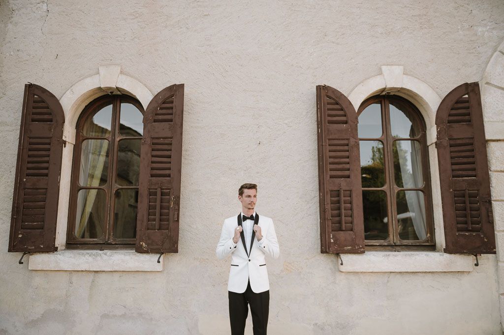 Symmetrical composition of groom in white tuxedo between two vintage windows.