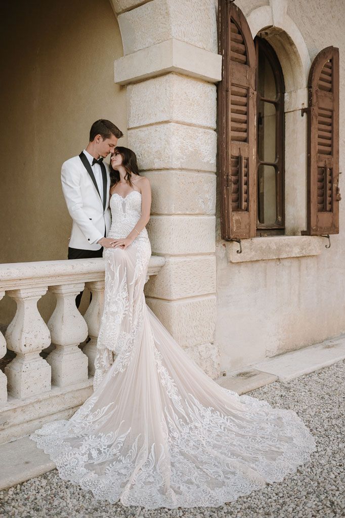 Bride and groom share intimate moment against villa wall with dramatic wedding dress train.