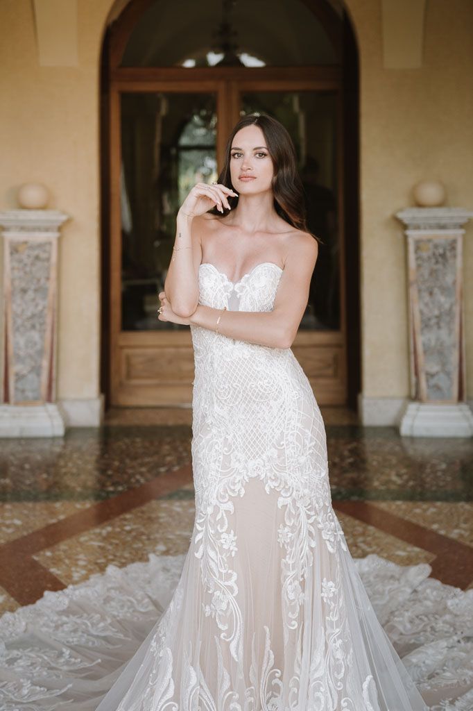 Full-length shot of bride in fitted lace gown with sweetheart neckline and cathedral train.