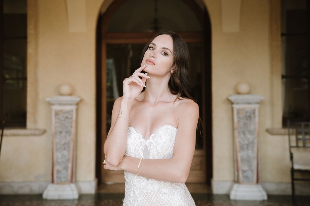 A bridal portrait featuring a delicate white lace dress in front of stone columns and arched doorway.