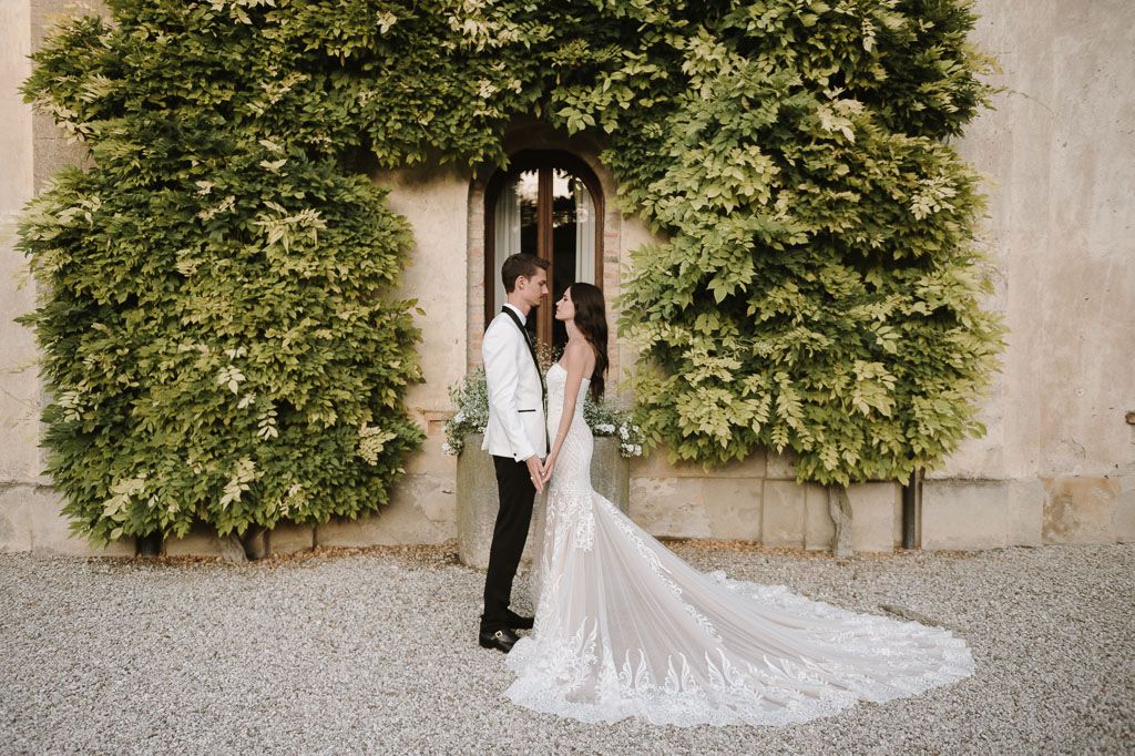 A romantic wedding photo of a couple framed by lush green vines against a stone wall.
