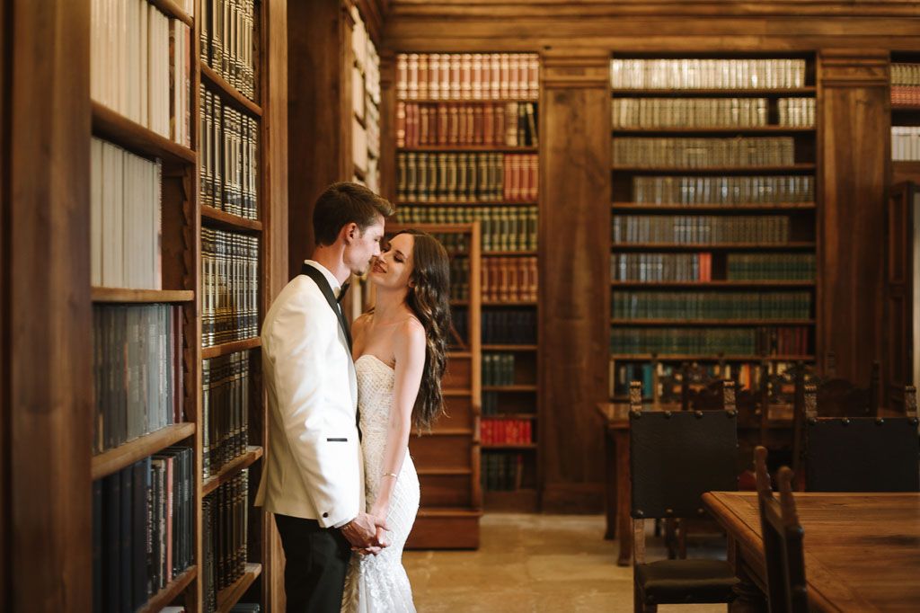 Romantic wedding couple shares an intimate moment against a backdrop of classic library books.
