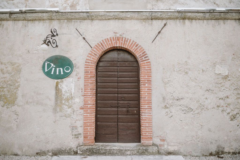 Rustic wooden door with brick arch frame and vintage 'Vino' sign on weathered wall.