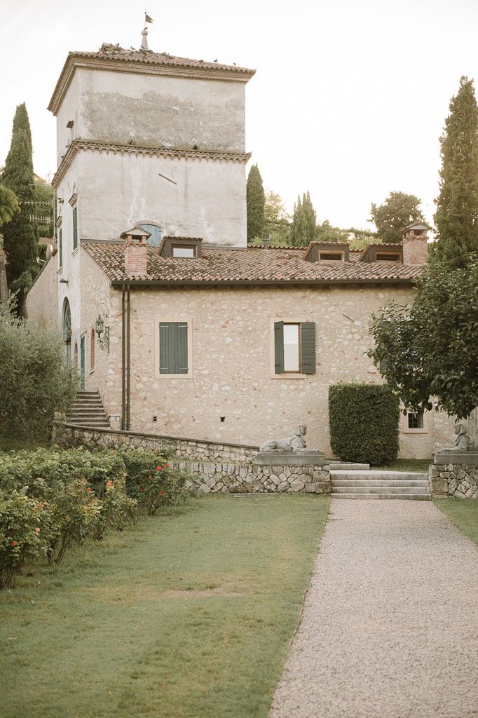 Historic Italian villa with stone tower and green shuttered windows amid manicured grounds.