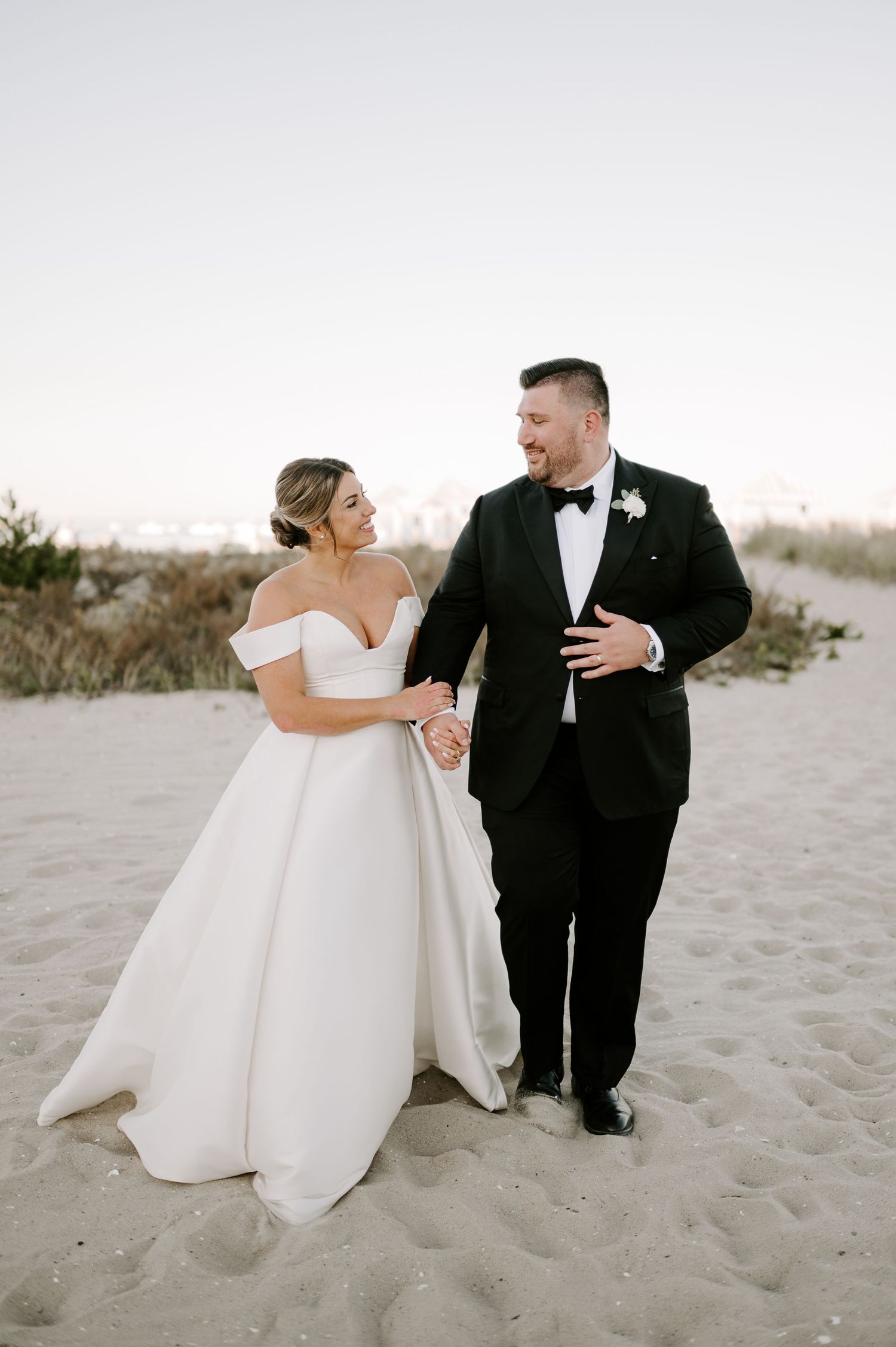 Newlyweds share intimate moment on sandy beach during wedding photoshoot.