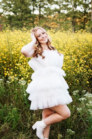 Playful portraits in a white ruffle dress surrounded by yellow wildflowers at sunset.