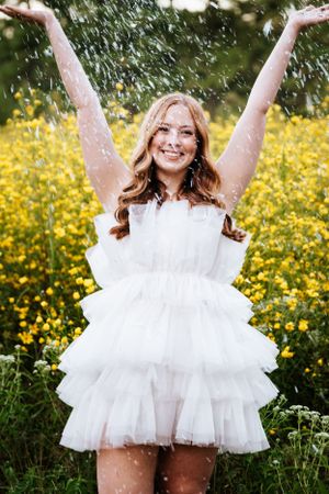 A joyful figure in a white tulle dress poses playfully in a field of yellow wildflowers.
