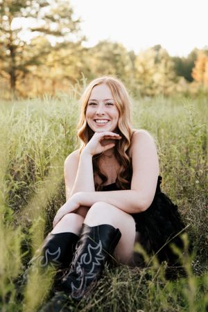 Candid outdoor portraits showing joyful expressions while sitting in tall grass wearing a black dress.