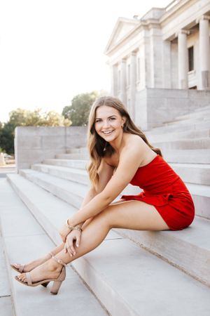 A red dress contrasts beautifully against white stone steps in an elegant outdoor photoshoot.