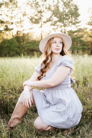 Dreamy outdoor portraits in a light blue dress and wide-brimmed hat among wildflowers.