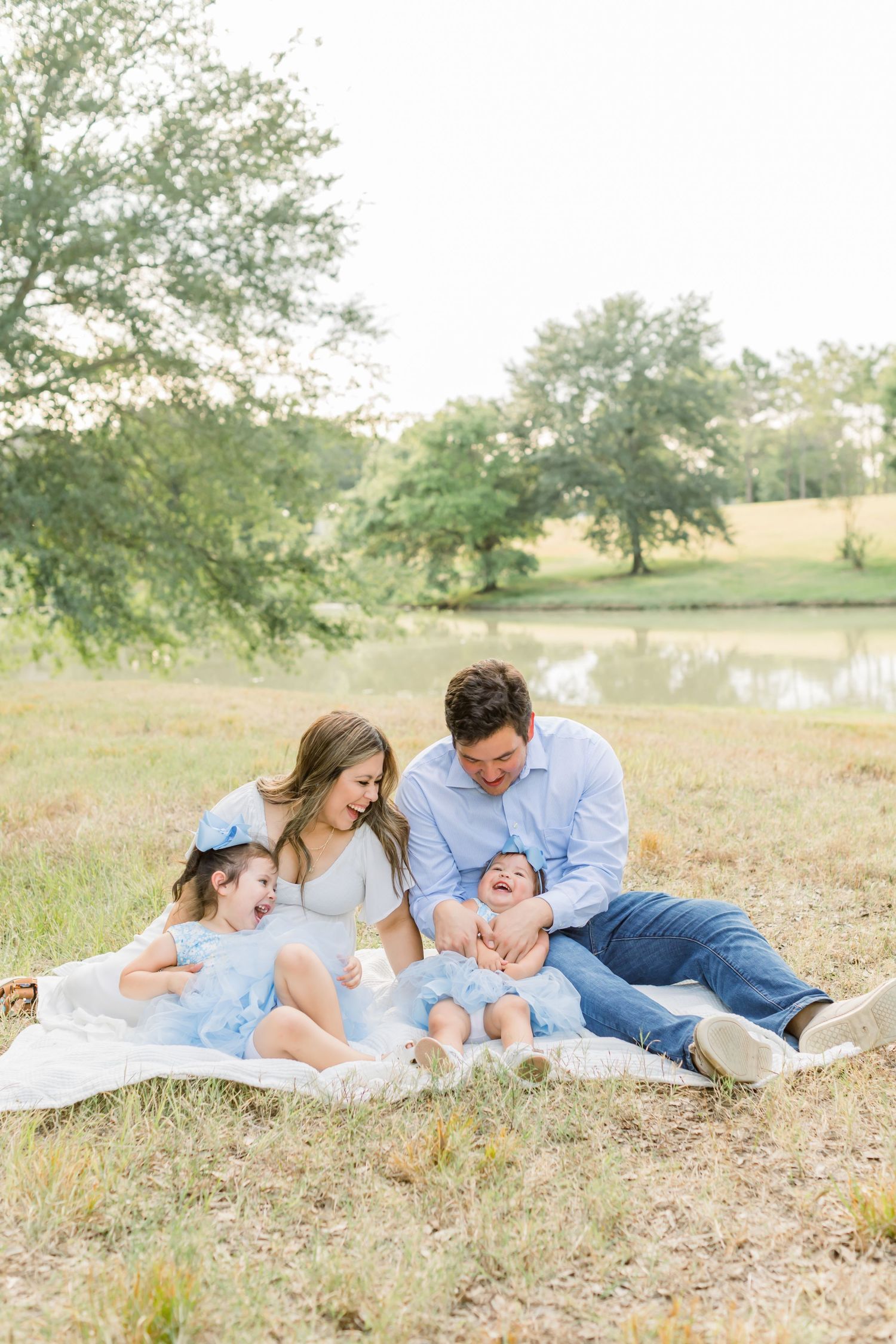 Intimate family portrait on white blanket in nature setting with pond view.