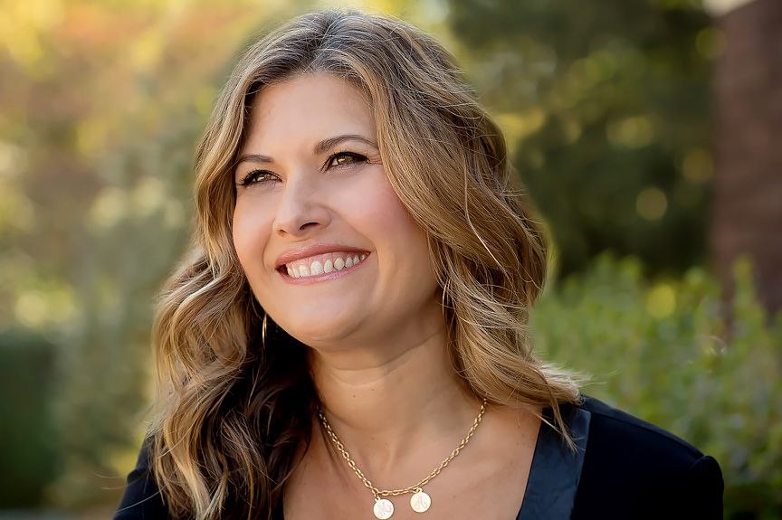 Natural outdoor portrait of woman with wavy brown hair smiling while looking up.