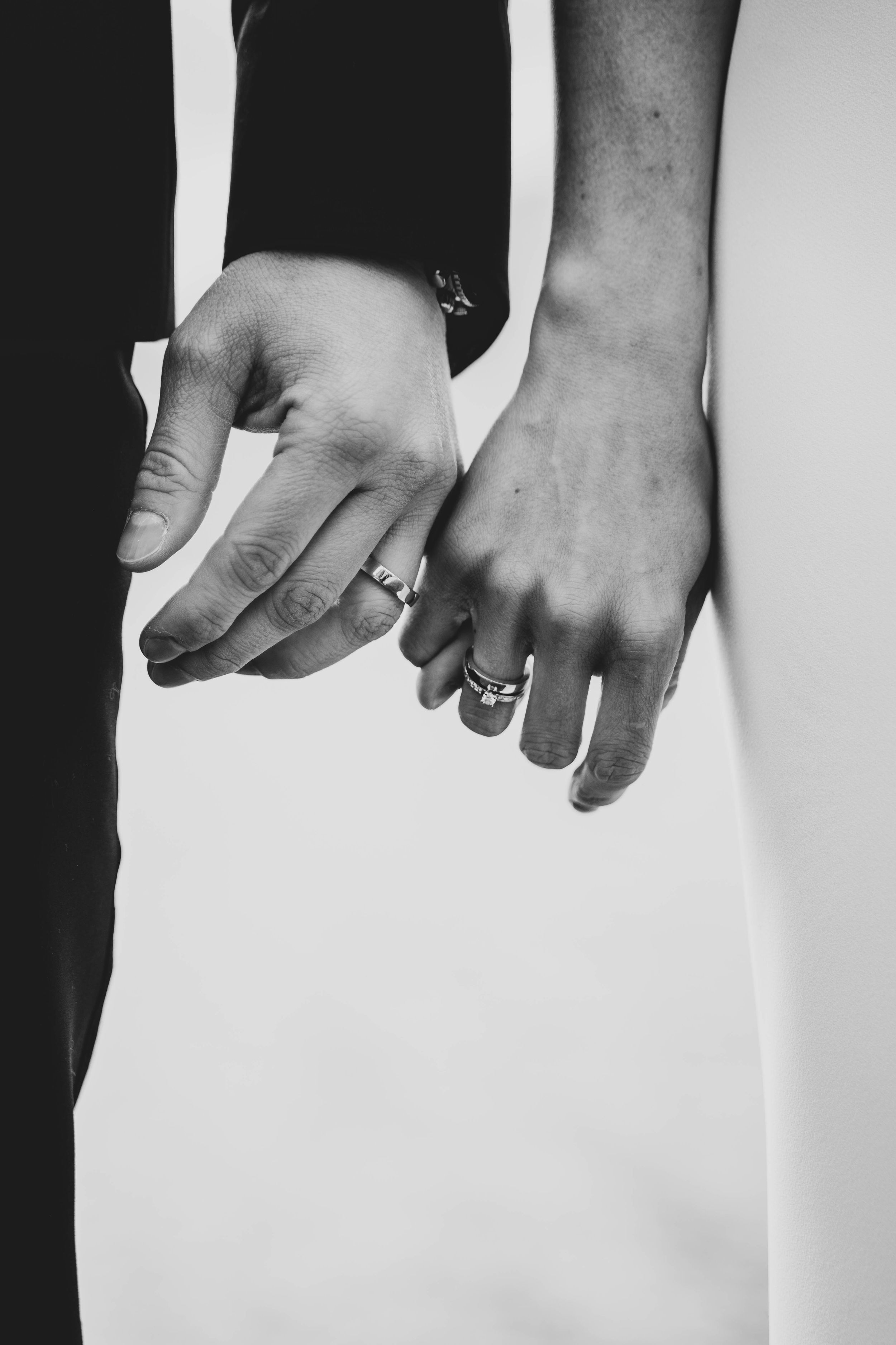 Close-up black and white photo of hands wearing wedding rings.