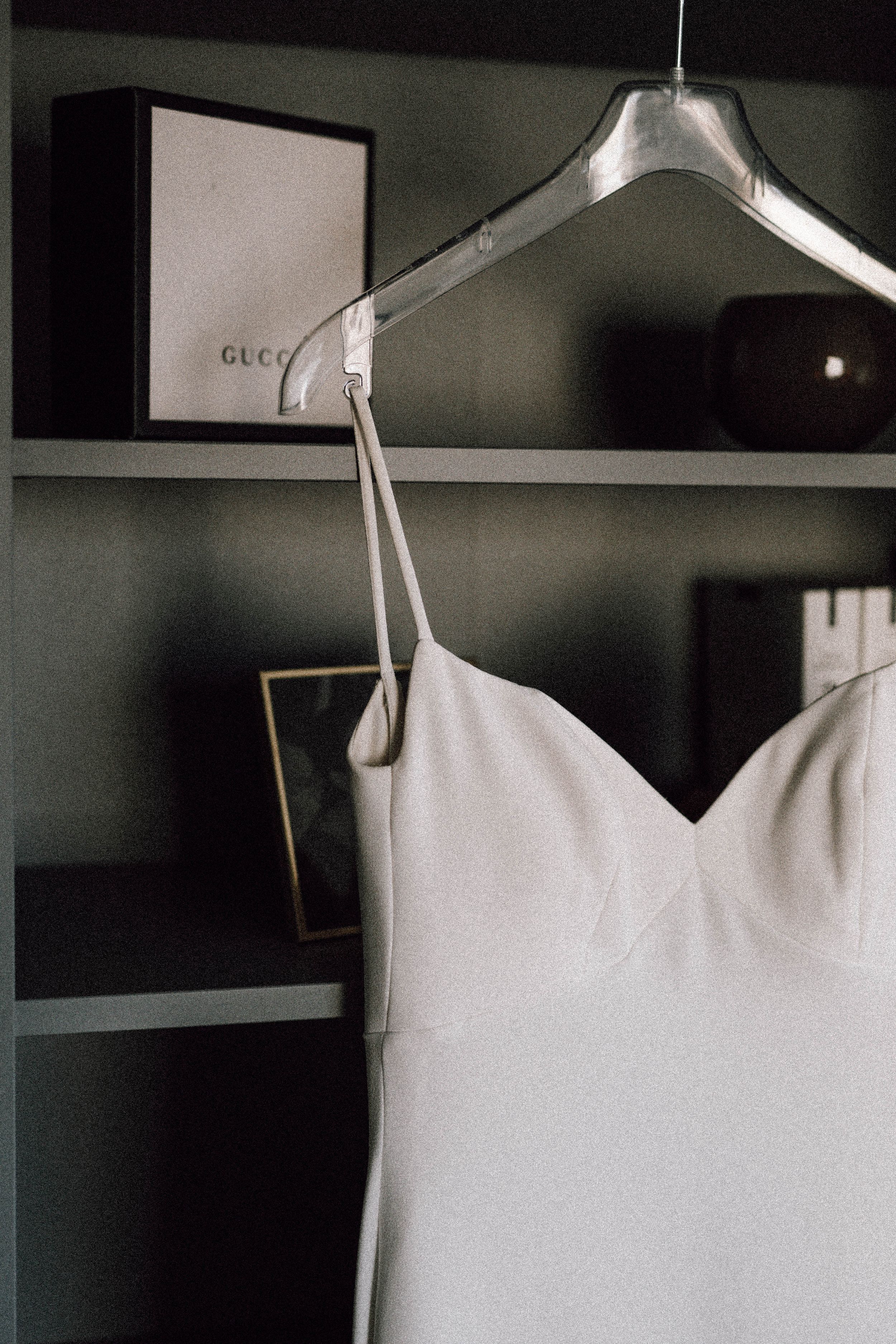 Elegant white wedding dress hanging on a silver hanger against a dark wall.