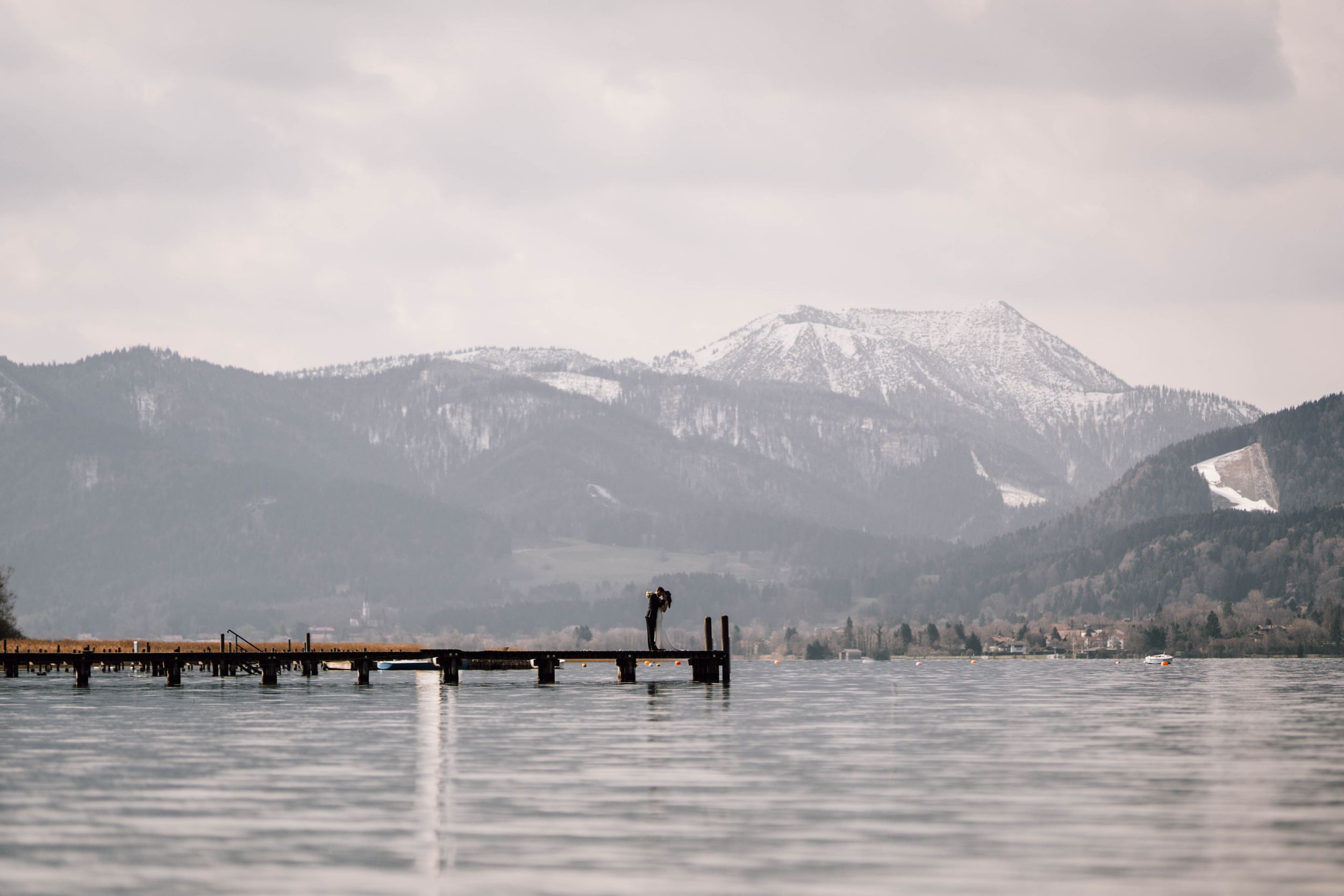 Panoramic view of a lake with mountains and a wooden pier in the distance.