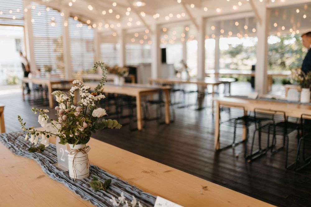 Elegant wedding reception hall with string lights, farm tables, and floral centerpieces in mason jars.