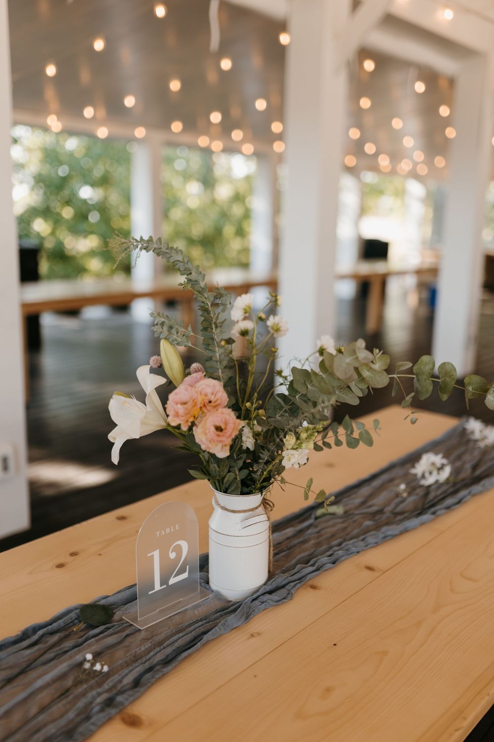 Table 12 centerpiece with pink and white flowers in mason jar on rustic wood runner with string lights.