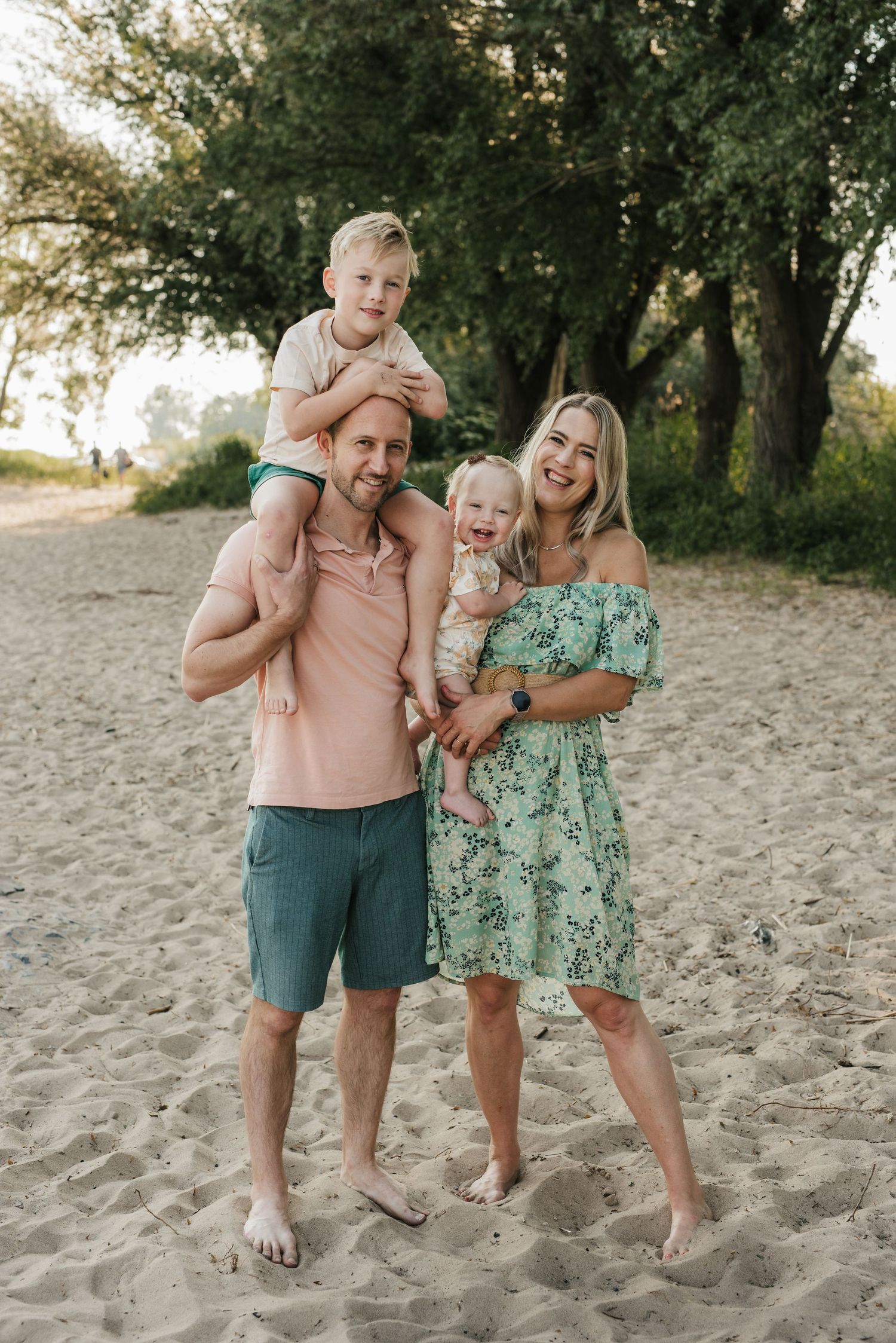 Family enjoying a sunny day together on a sandy beach with trees in the background.