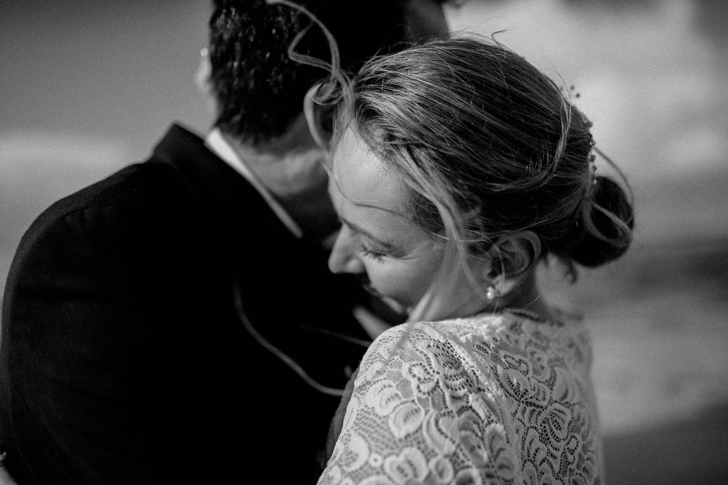 Black and white wedding photo showing couple in intimate moment with bride wearing delicate lace gown.