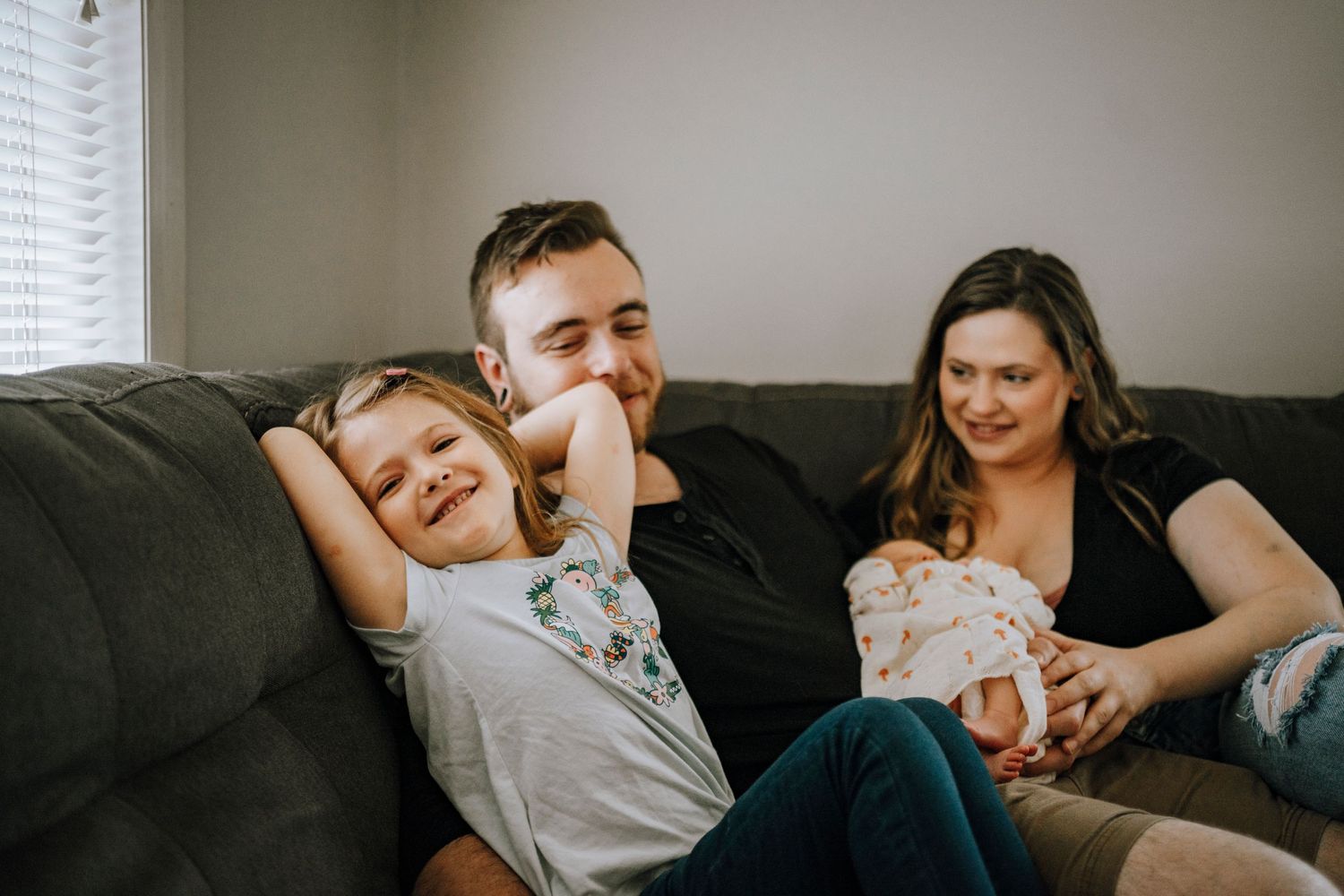 Candid moment of family laughing together on couch while holding newborn.