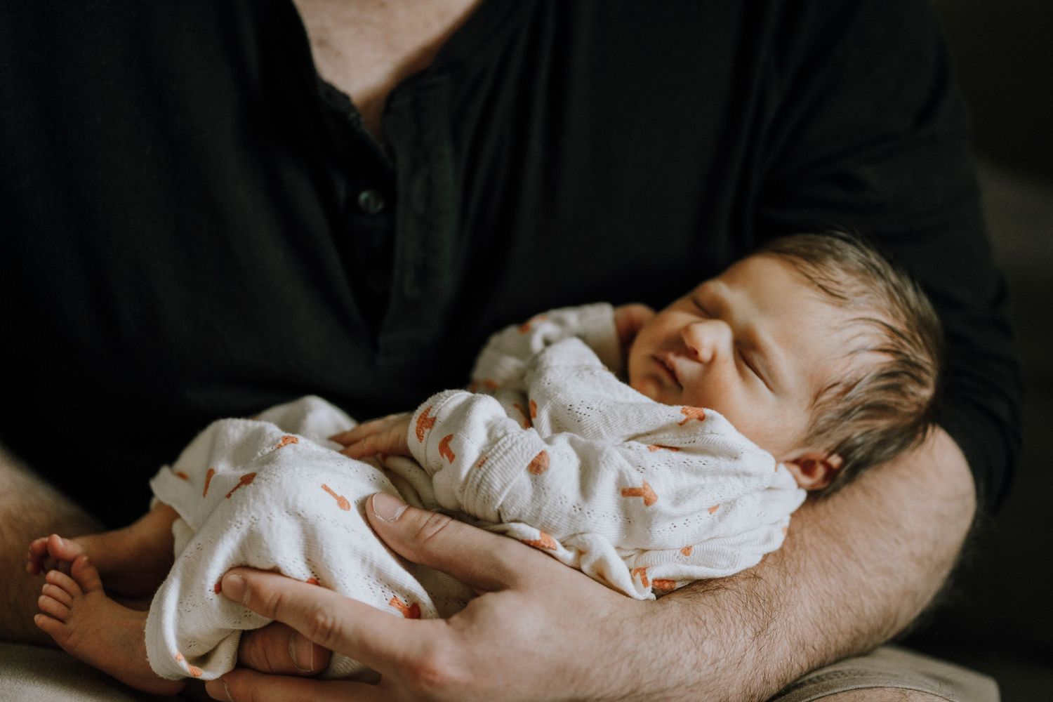 Newborn baby sleeping peacefully in white onesie while being cradled.