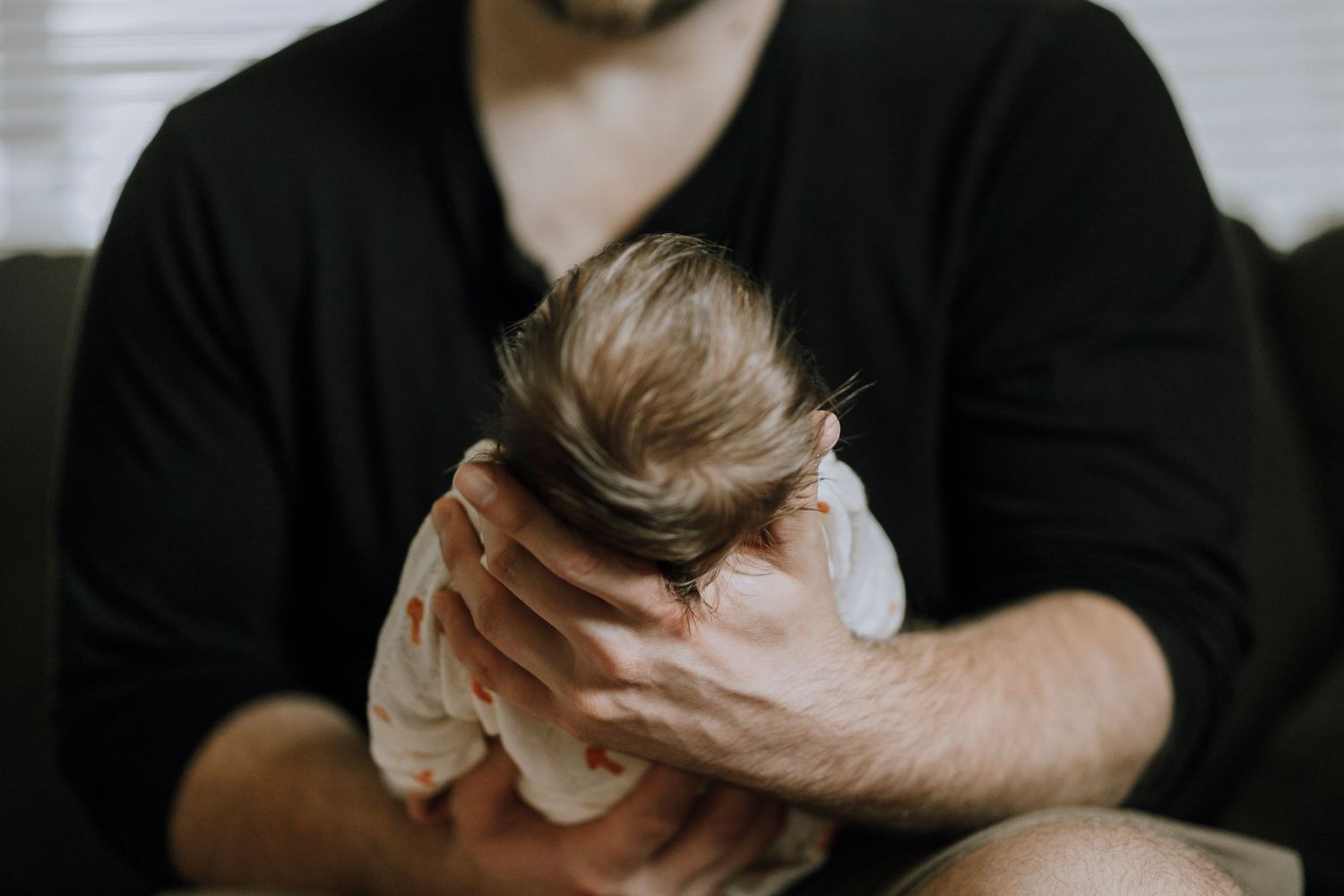 Close-up view of newborn baby being held in parent's arms wearing white clothing.