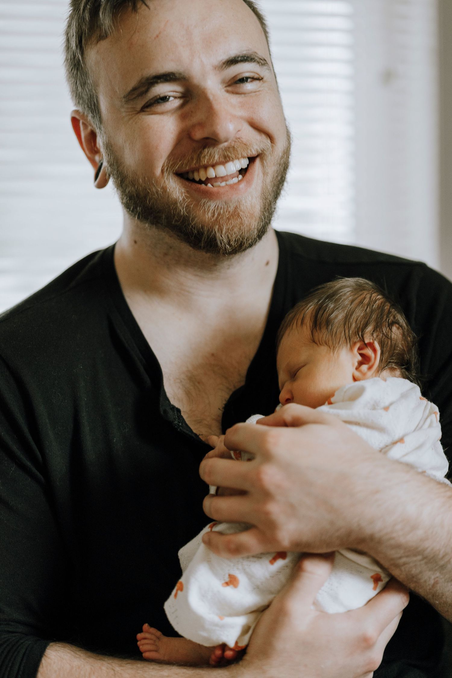 Parent holding newborn baby in white onesie while smiling warmly.