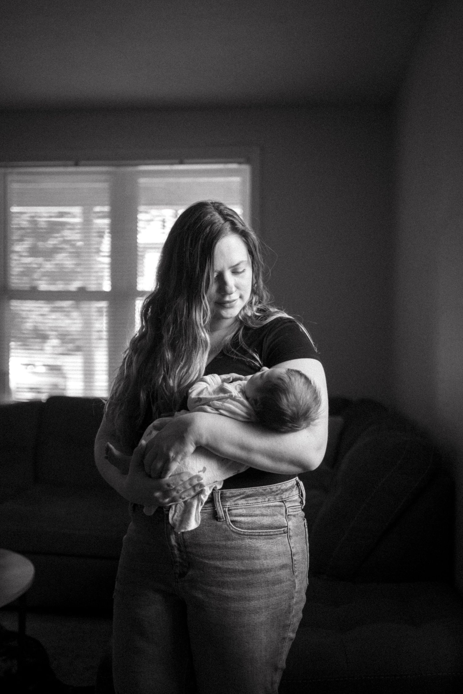 Black and white portrait of parent holding sleeping newborn in living room with natural light.