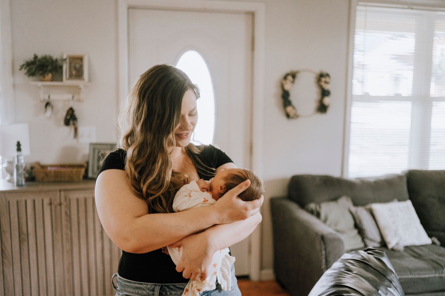 Parent cradling newborn baby in bright, cozy home interior.