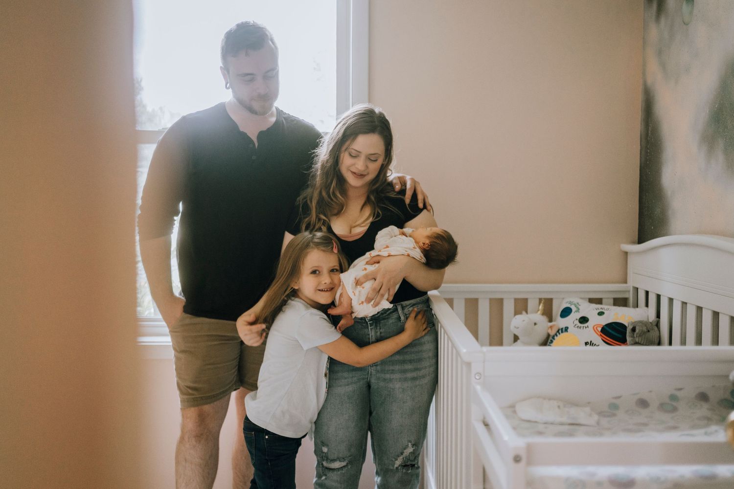 Family gathered together in nursery room with newborn baby and young sibling.