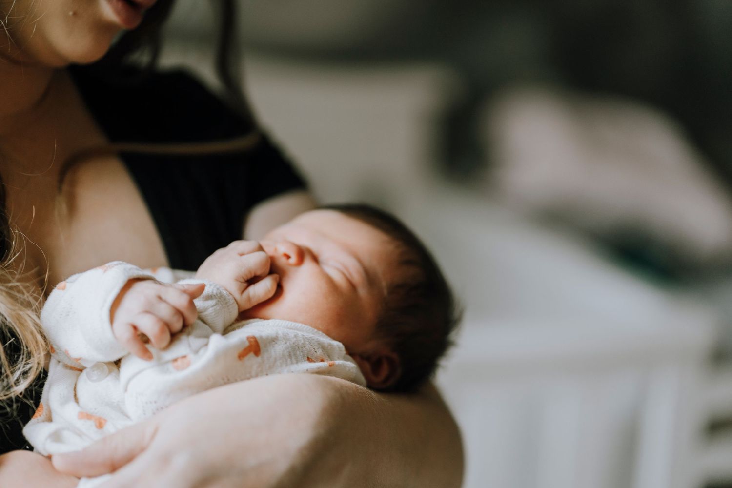 Newborn in white clothing sleeping peacefully against caregiver.
