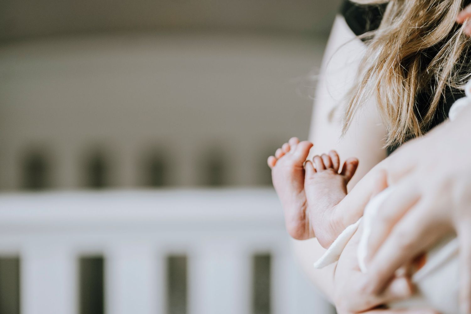 Tiny baby feet being held gently against white crib railing.