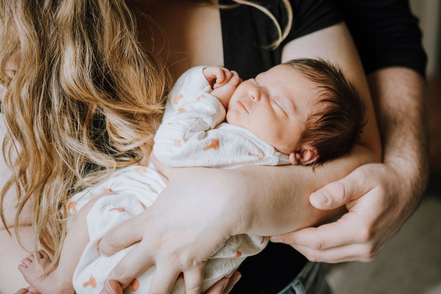 Intimate portrait of newborn being held against dark clothing.