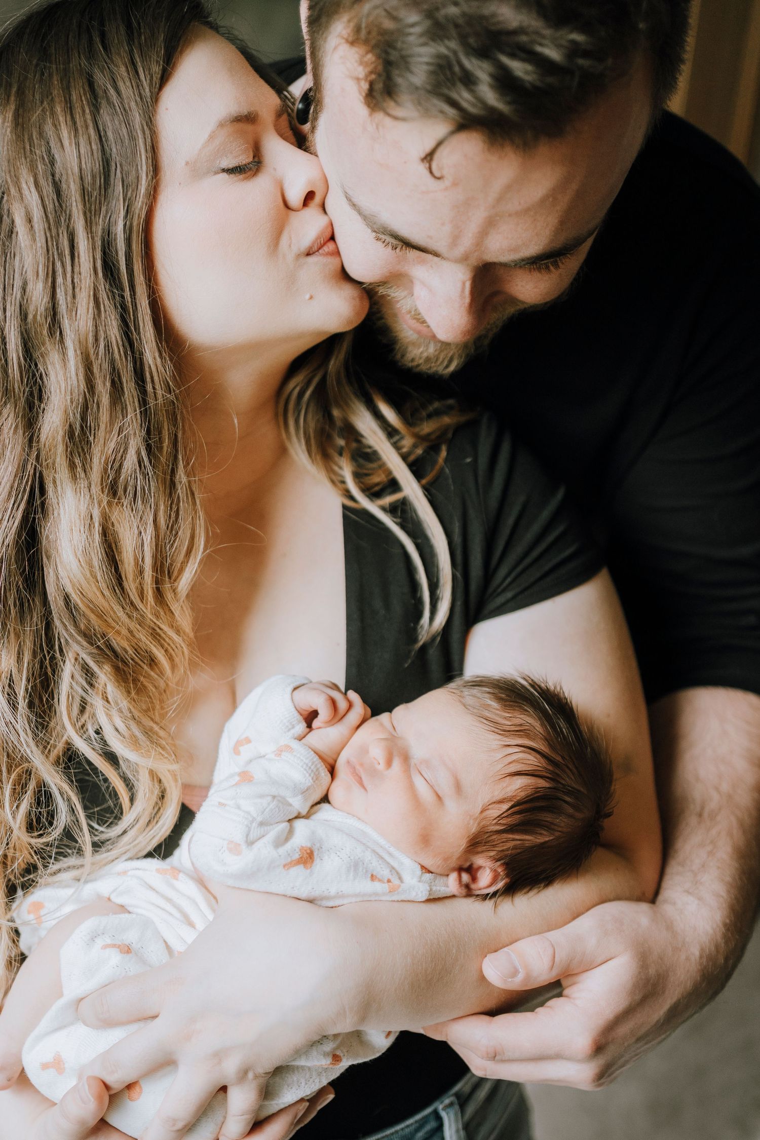 Intimate family moment with sleeping newborn held close.