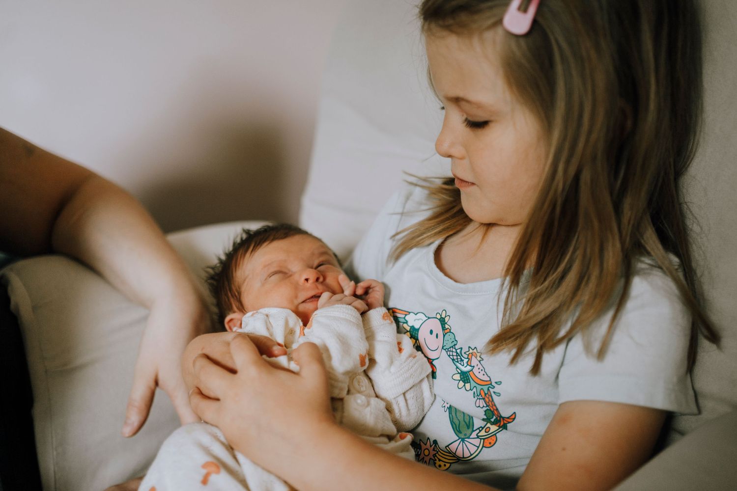 Young child holding and gazing at sleeping newborn.